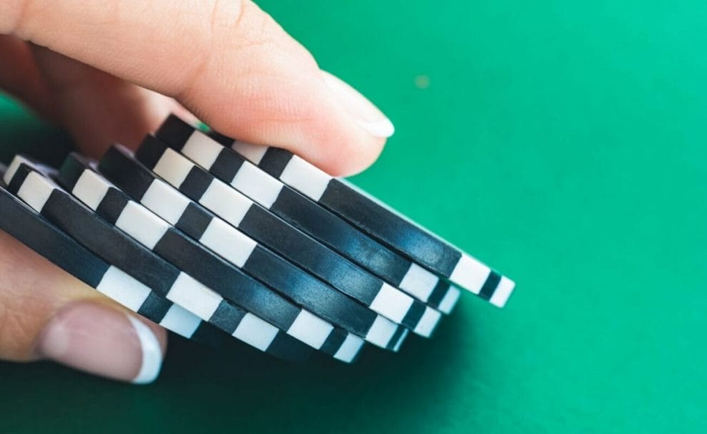  A manicured hand holds black casino chips over a green background.