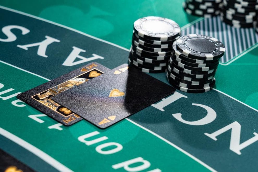 Two black playing cards feature alongside black casino chips on a blackjack table.