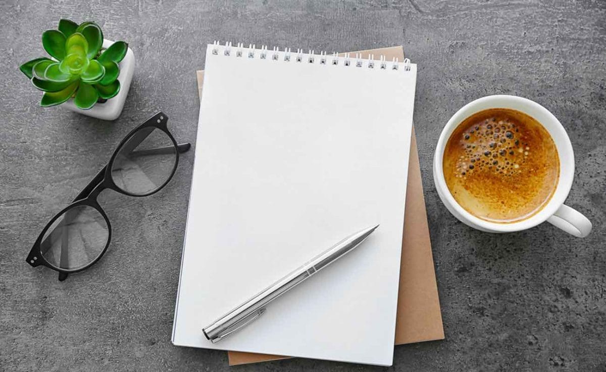 A notebook, pair of glasses and cup of coffee on a table.