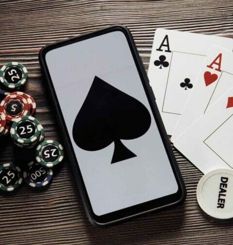 Playing cards and casino chips on either side of a smartphone that displays a spade.