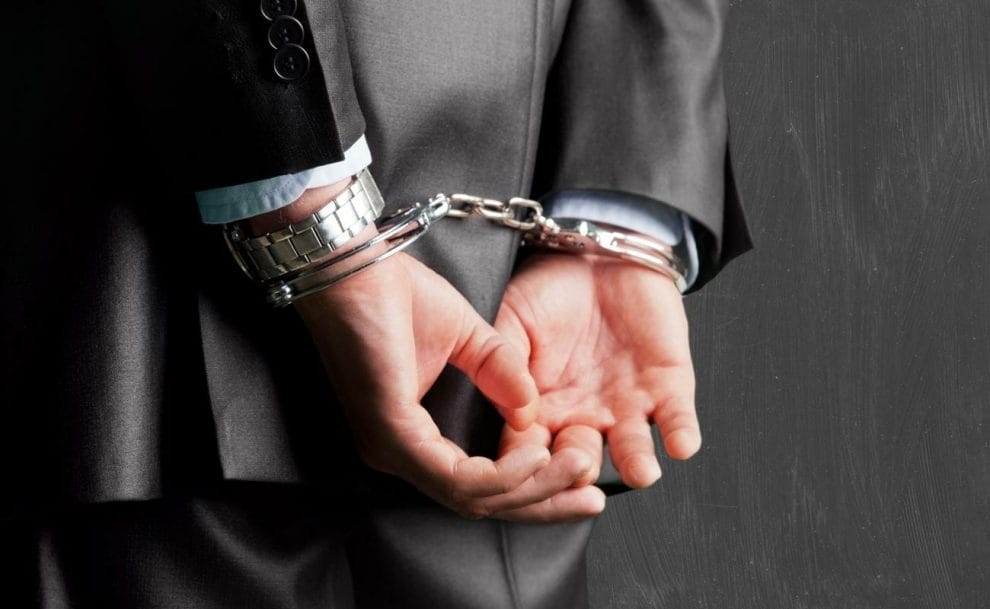 A man in a business suit with his hands behind his back in handcuffs.