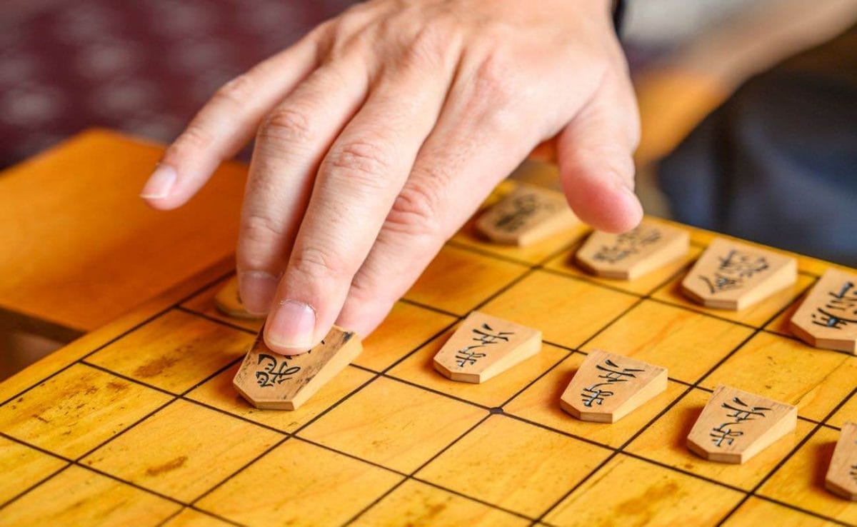 A hand moves a piece on a shogi board.