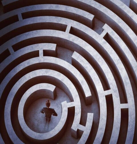 A person in a suit stands in the center of a maze.