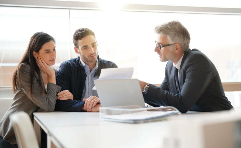 A young couple talking to a financial advisor at a table with a laptop and documents.