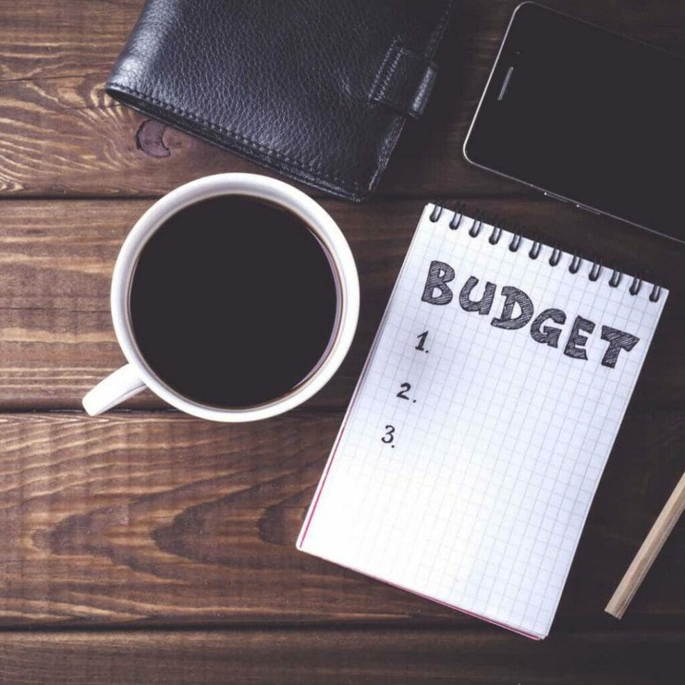 A cup of coffee, a phone and a notebook reading “budget”.