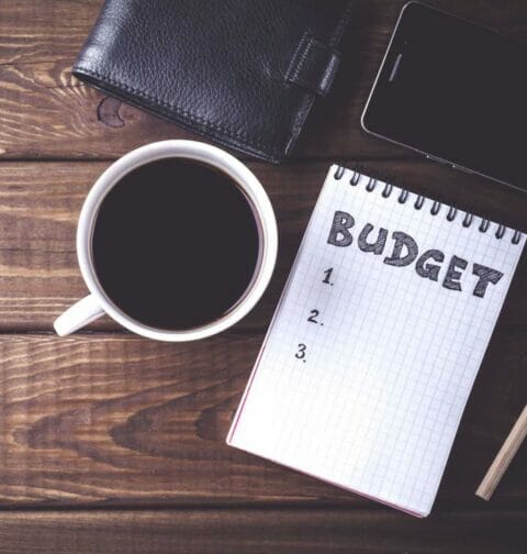 A cup of coffee, a phone and a notebook reading “budget”.
