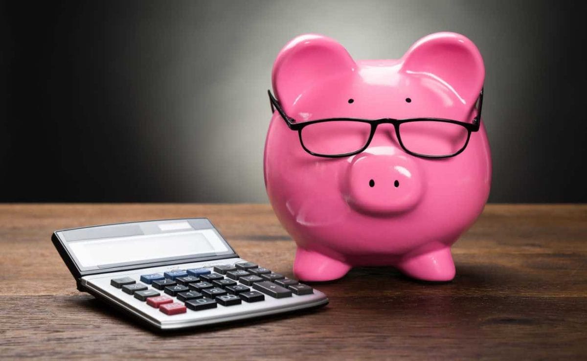 A piggy bank with glasses standing next to a calculator.