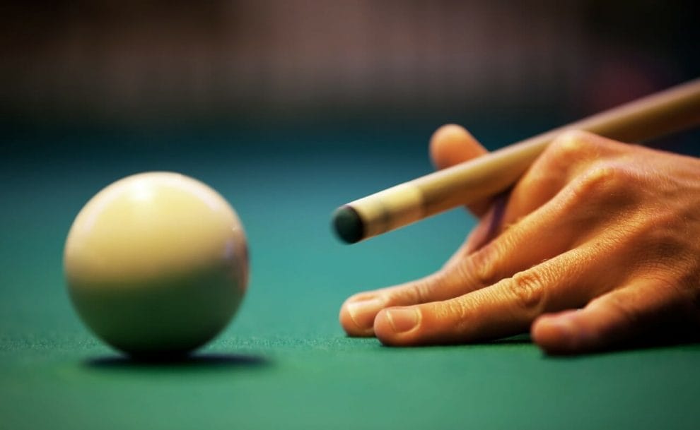 A snooker player’s hand with a cue stick aimed at the white ball.