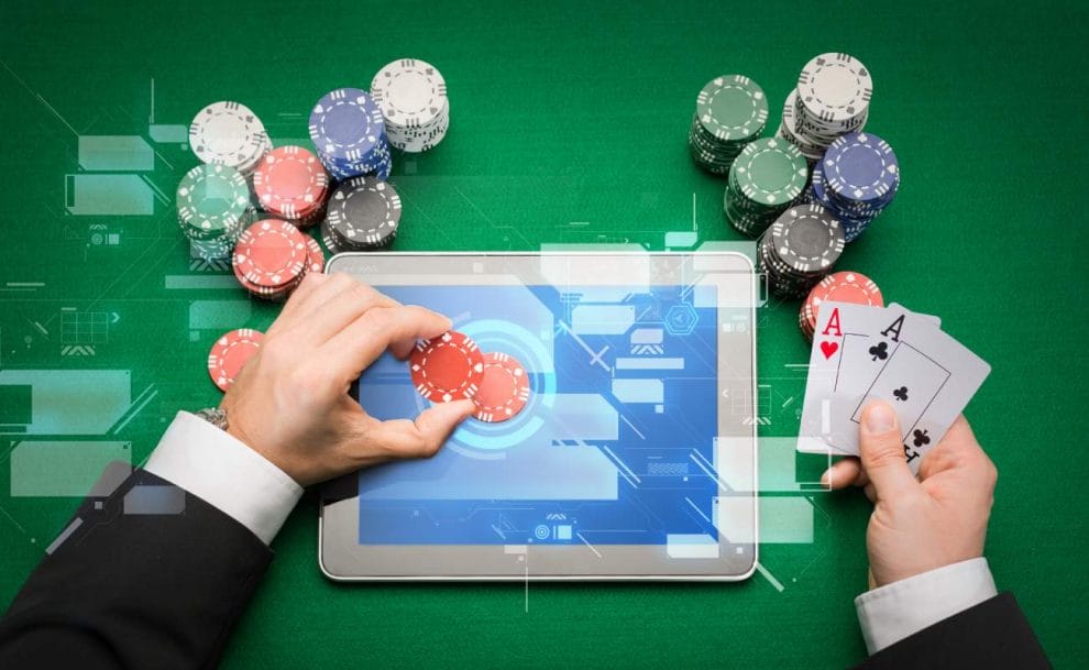 A man places a casino chip on a tablet with playing cards in his right hand.