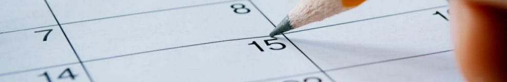 A person writing on a calendar with a pencil.