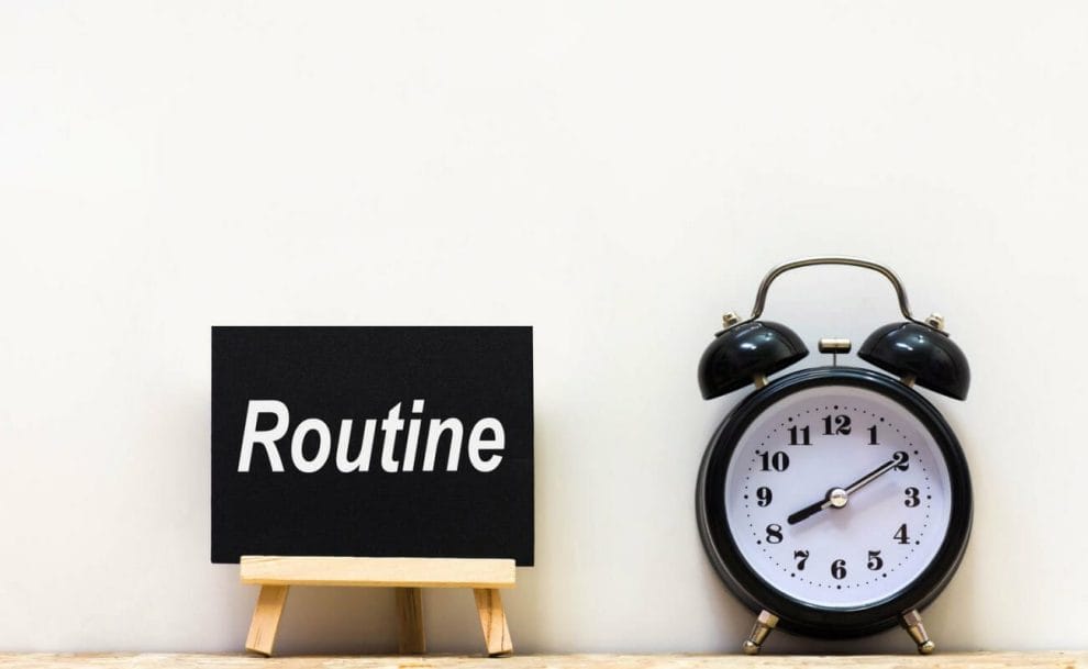 An alarm clock next to a small blackboard with the word “Routine” on it