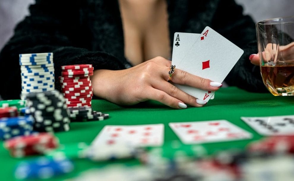 A female poker player reveals her hole cards while holding a drink. 