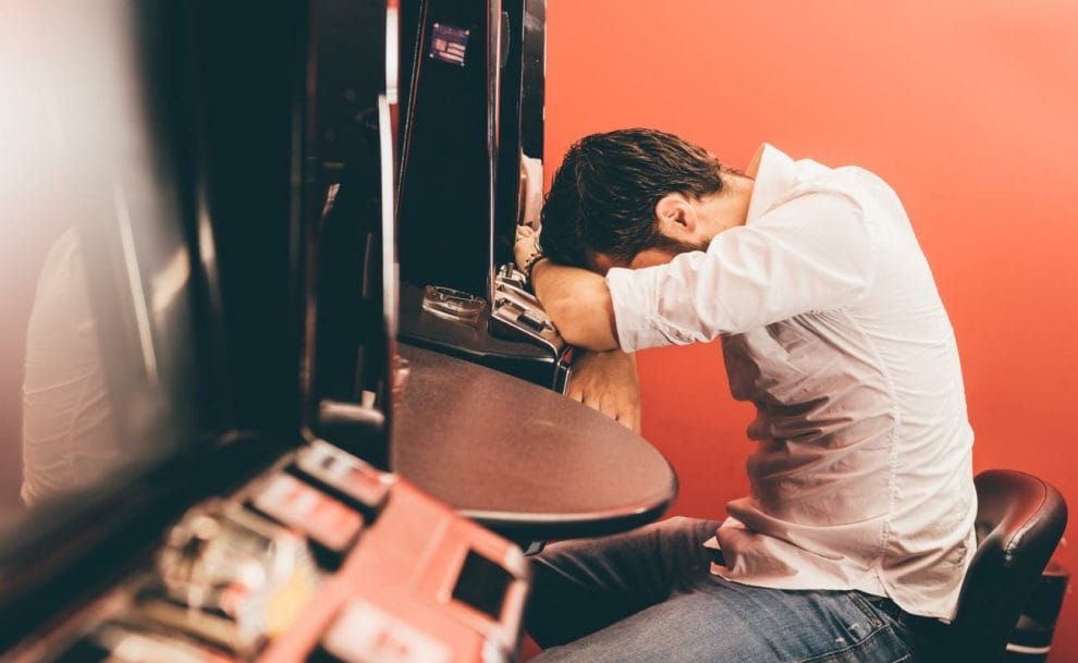 A man resting his head on a slot machine.