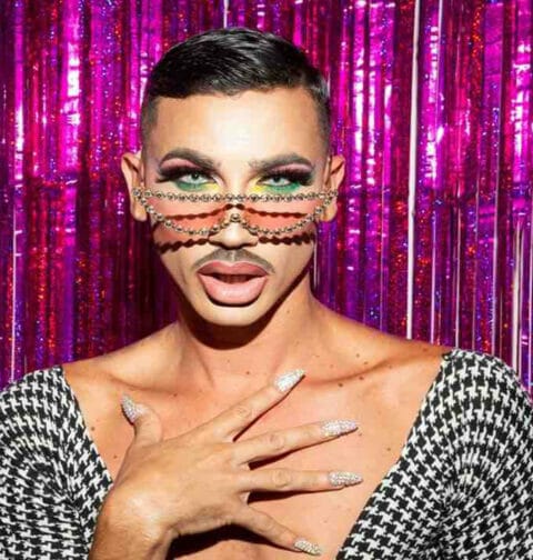 A drag queen’s face against a sparkly background.
