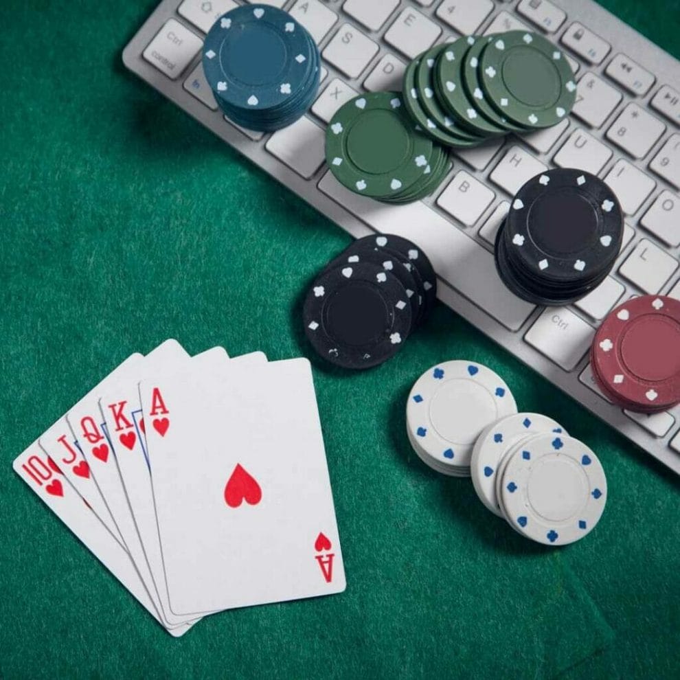 A royal flush hand sits on a poker table next to poker chips and a computer keyboard.