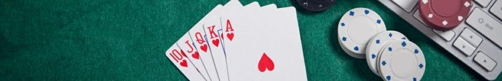 A royal flush hand sits on a poker table next to poker chips and a computer keyboard.