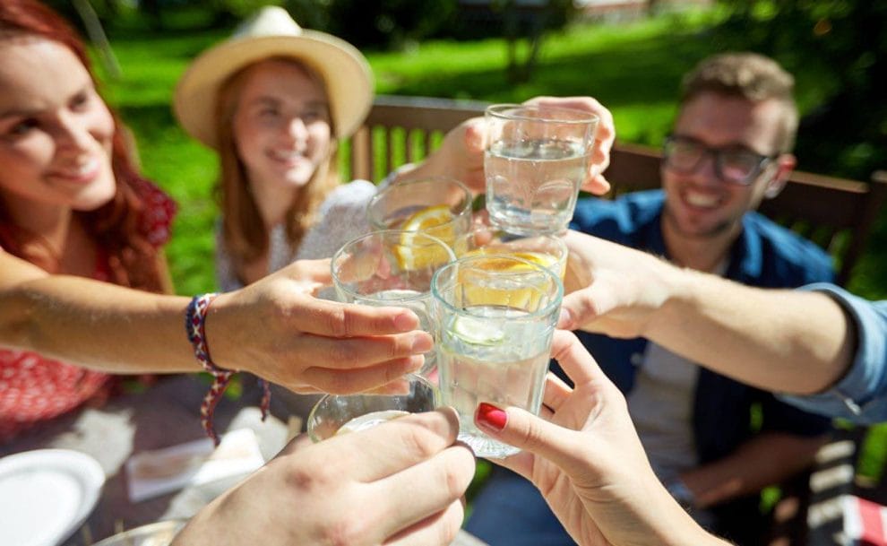 A group of friends toasting with glasses of lemon water.