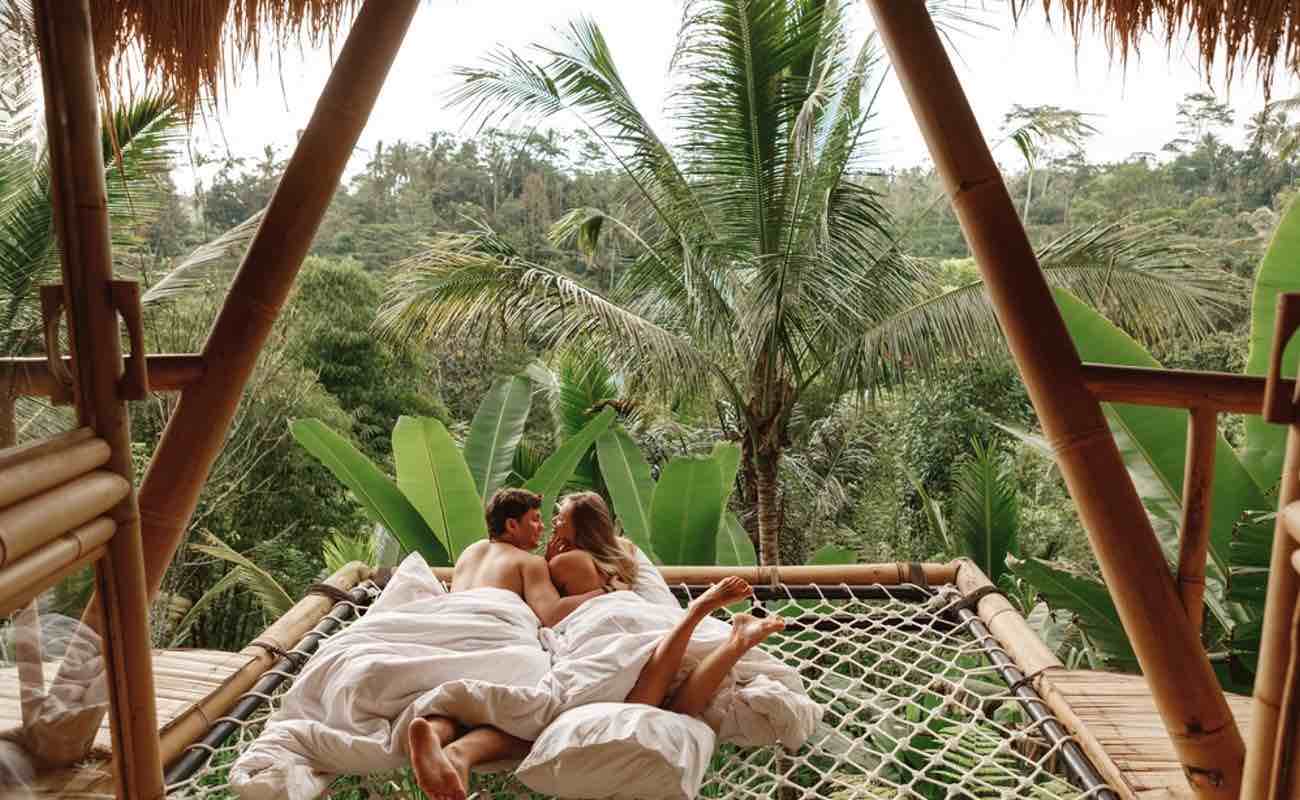 A couple relaxes in a luxury tree house overlooking a jungle landscape.