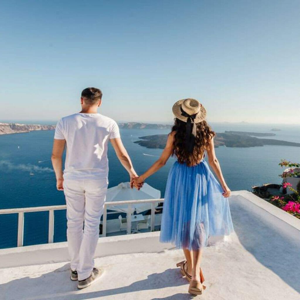 A couple holds hands while looking at the ocean view in Santorini, Greece.