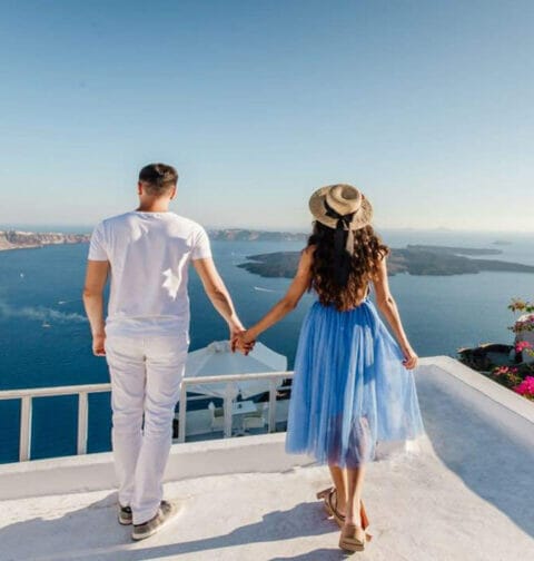 A couple holds hands while looking at the ocean view in Santorini, Greece.