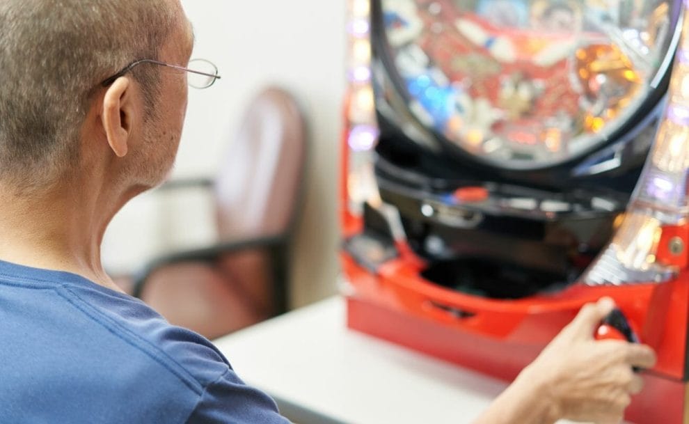 An older man wearing glasses playing pachinko.