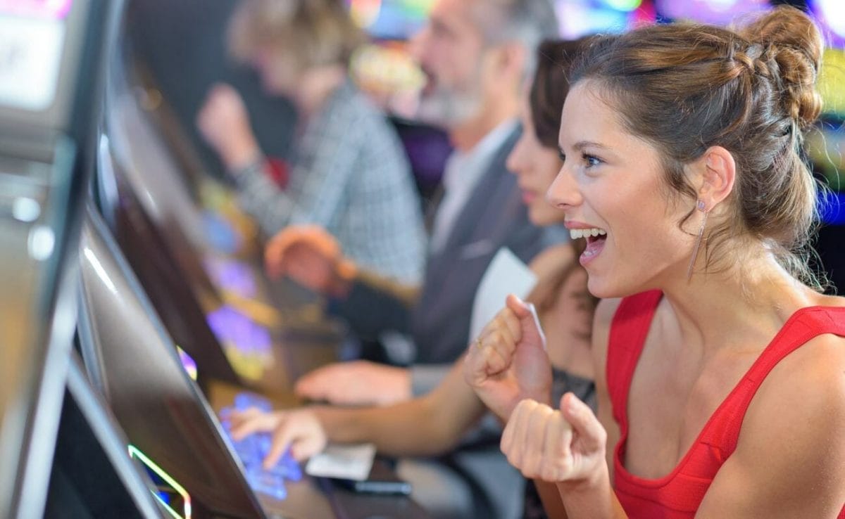A woman in a red dress playing slots clenches her hands in excitement.