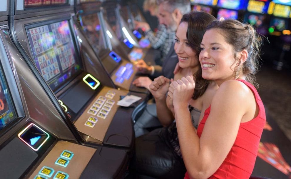 Two women clench their fists in anticipation while playing a slot machine.
