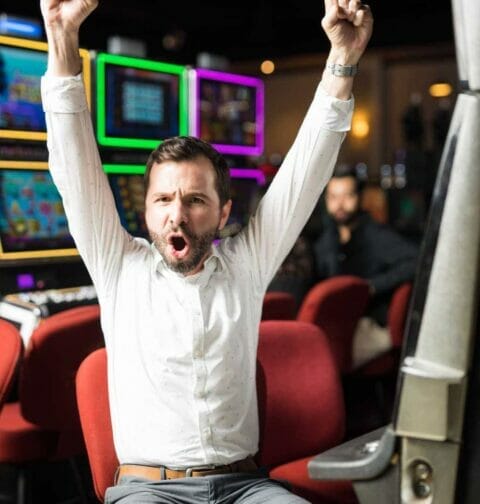 A man celebrates while sitting at a slot machine.