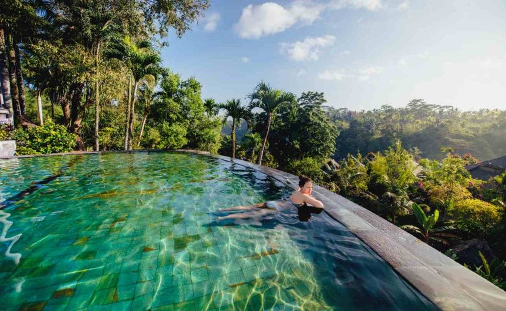 A person relaxes in a pool surrounded by trees.