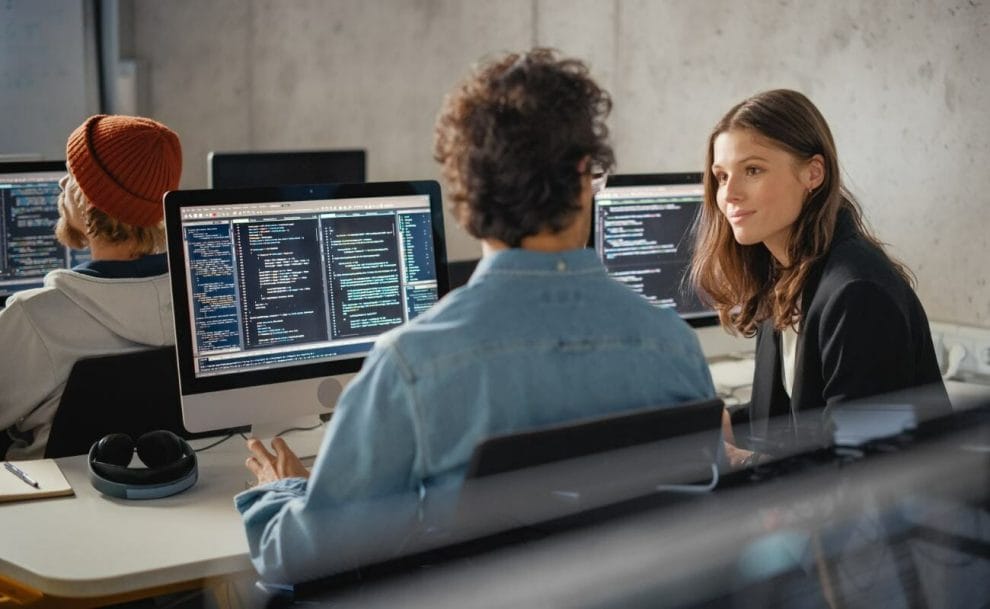 Co-workers sit in front of computers with code on the screens.