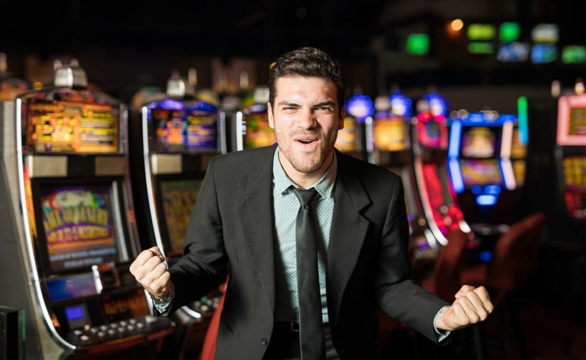 A man in a suit celebrating in front of a row of slot machines.