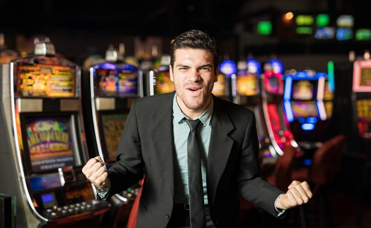 A man in a suit celebrating in front of a row of slot machines.