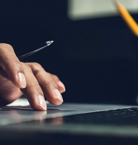 A hand holding a pen and moving on the touchpad of a laptop.