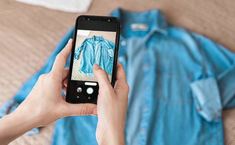 A woman taking a photo of a denim shirt with a smartphone.