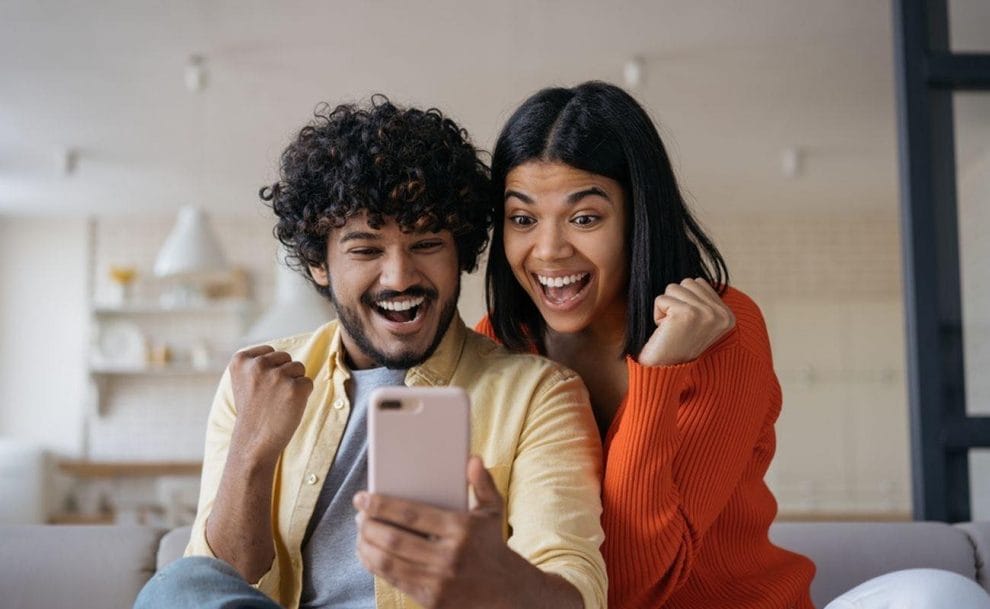 A couple celebrating a win while looking at a smartphone screen.