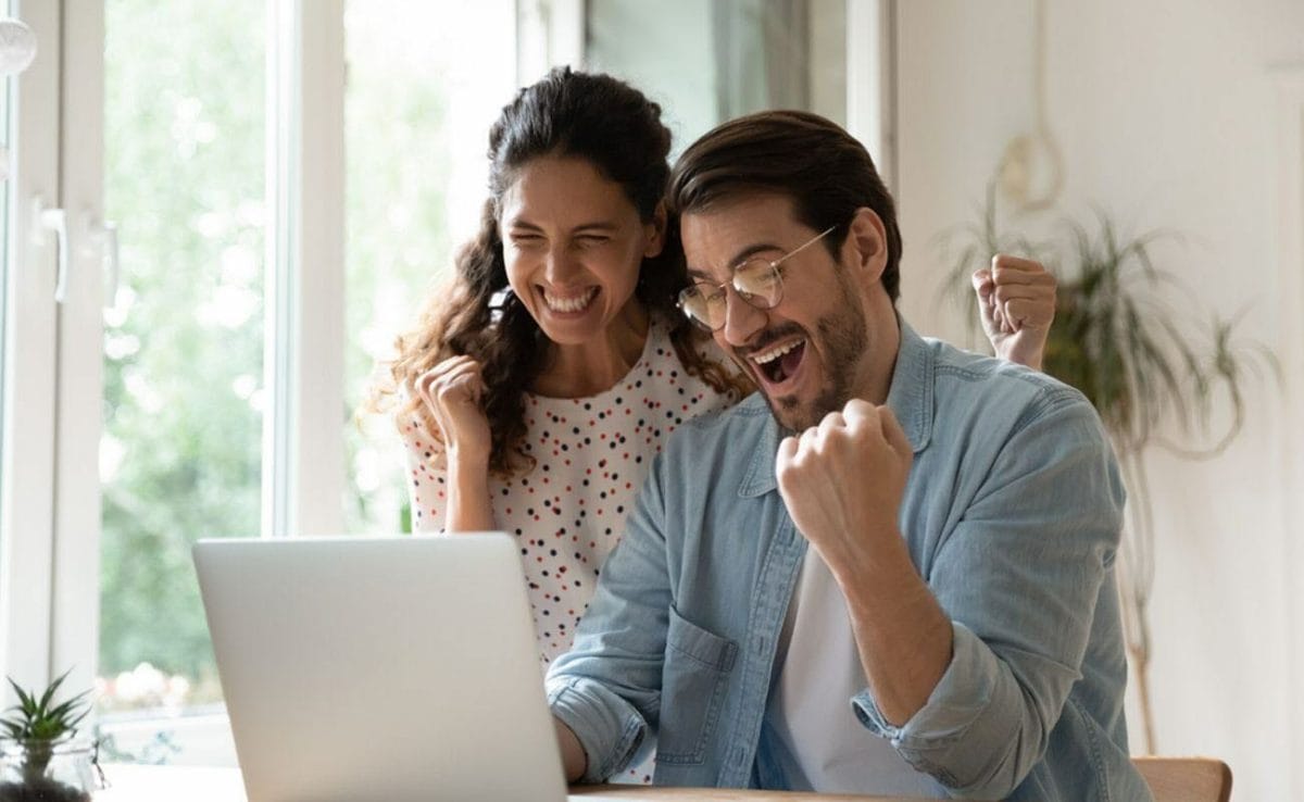 A couple celebrates while looking at a laptop screen.