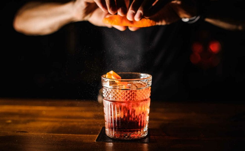 A bartender squeezes an orange peel into an Old Fashioned cocktail.