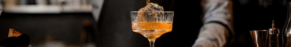 An orange cocktail in a decorative glass against a black background.
