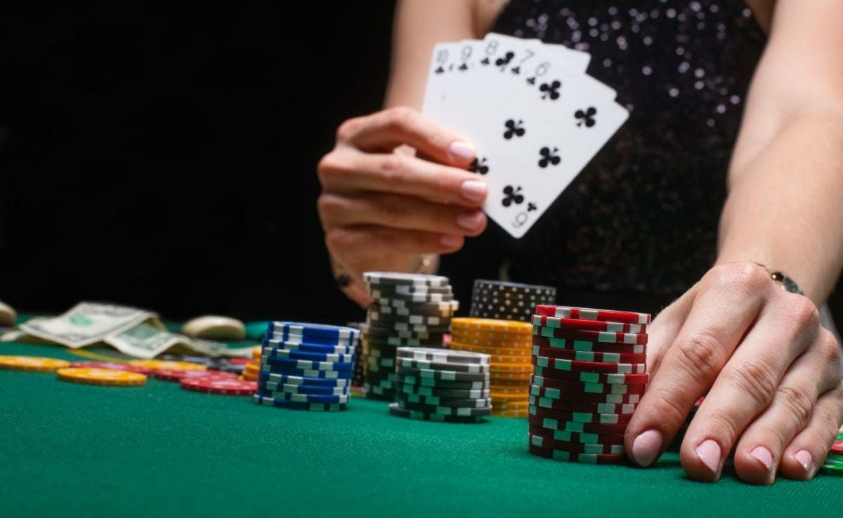 A person holding poker cards in one hand moves red casino chips with the other.