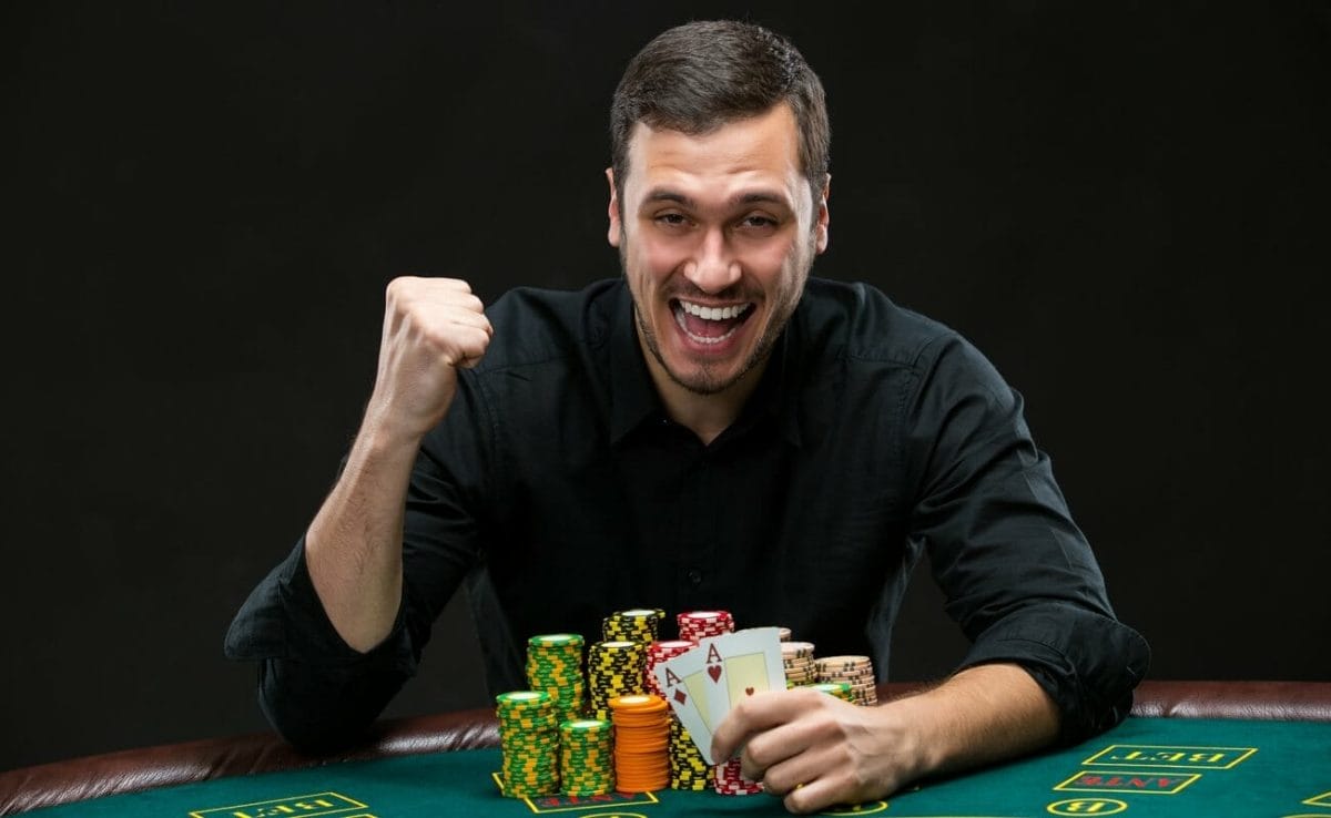 A poker player reveals his two aces and raises his fist in celebration.