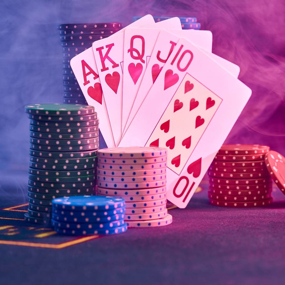A royal flush leaning against stacks of poker chips in a smoky room.
