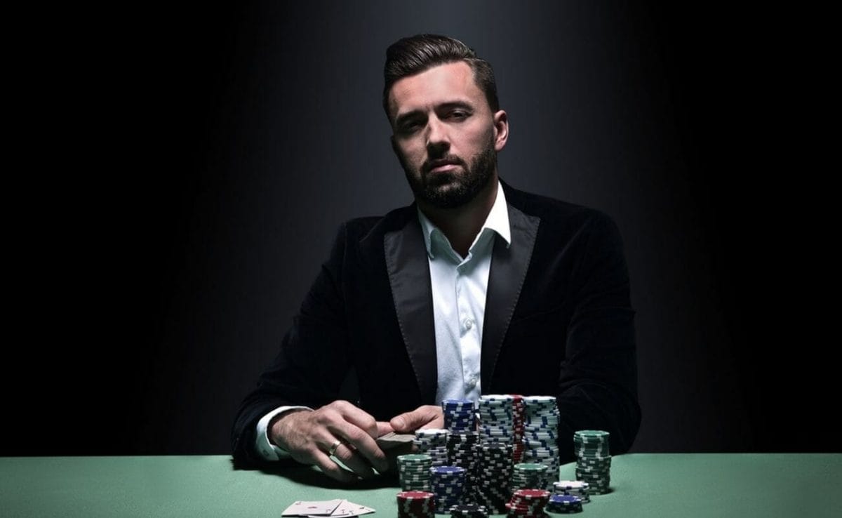 A man wearing a suit sitting at a poker table with large stacks of casino chips in front of him.