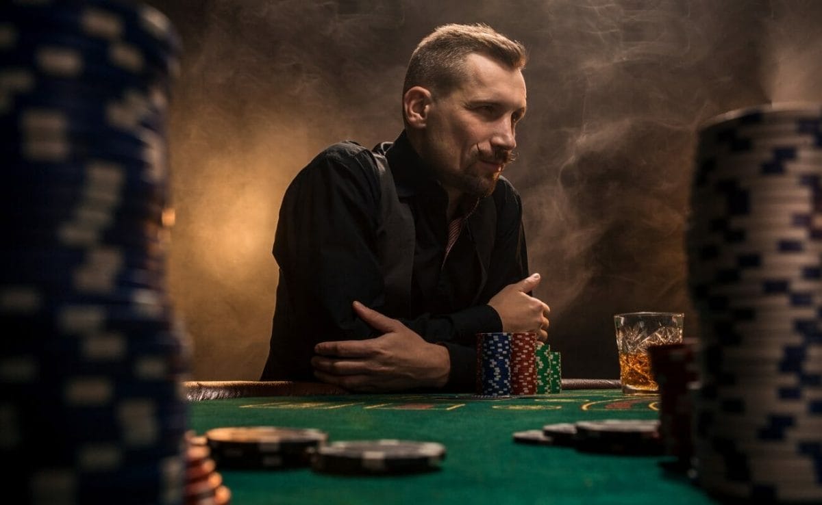 A well-dressed gambler with a curled mustache and a goatee thinks about their next play in a game of poker.