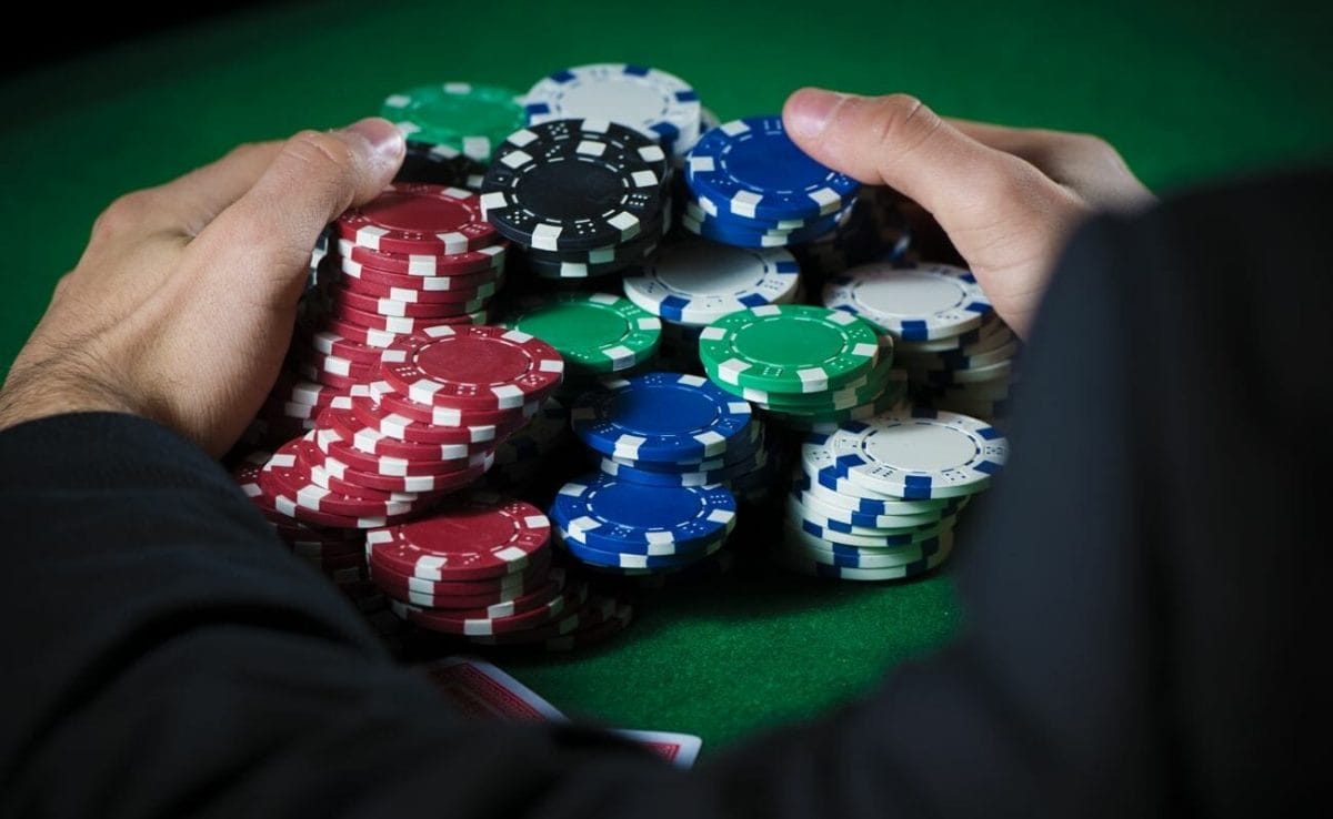 A person wearing a jacket pulling stacks of poker chips towards themselves.