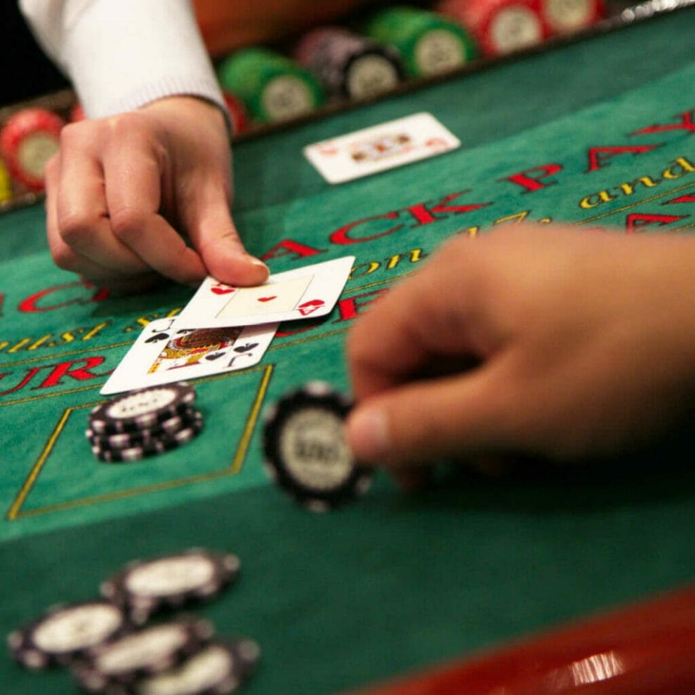 A dealer puts a card on the table while a player holds a chip.