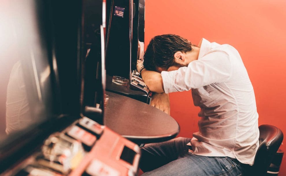 A person rests their head on a slot machine.