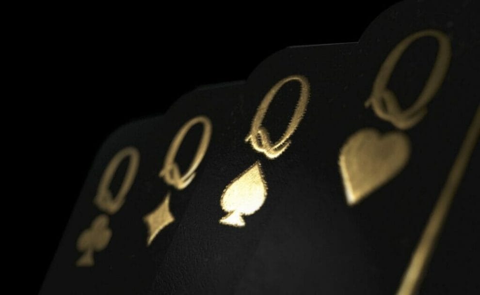 A group of four black playing cards with gold font and symbols. All four cards are queens.