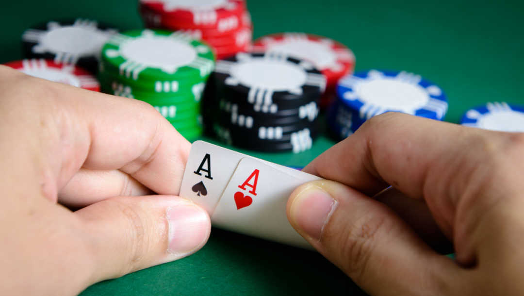 A person looks at two Ace cards in their hand with poker chips in the background