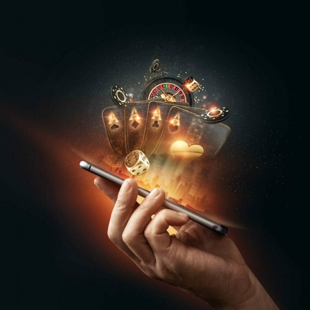 Online Gambling concept photograph, a man’s hand holding a mobile phone with gold accented gambling concepts being reflected