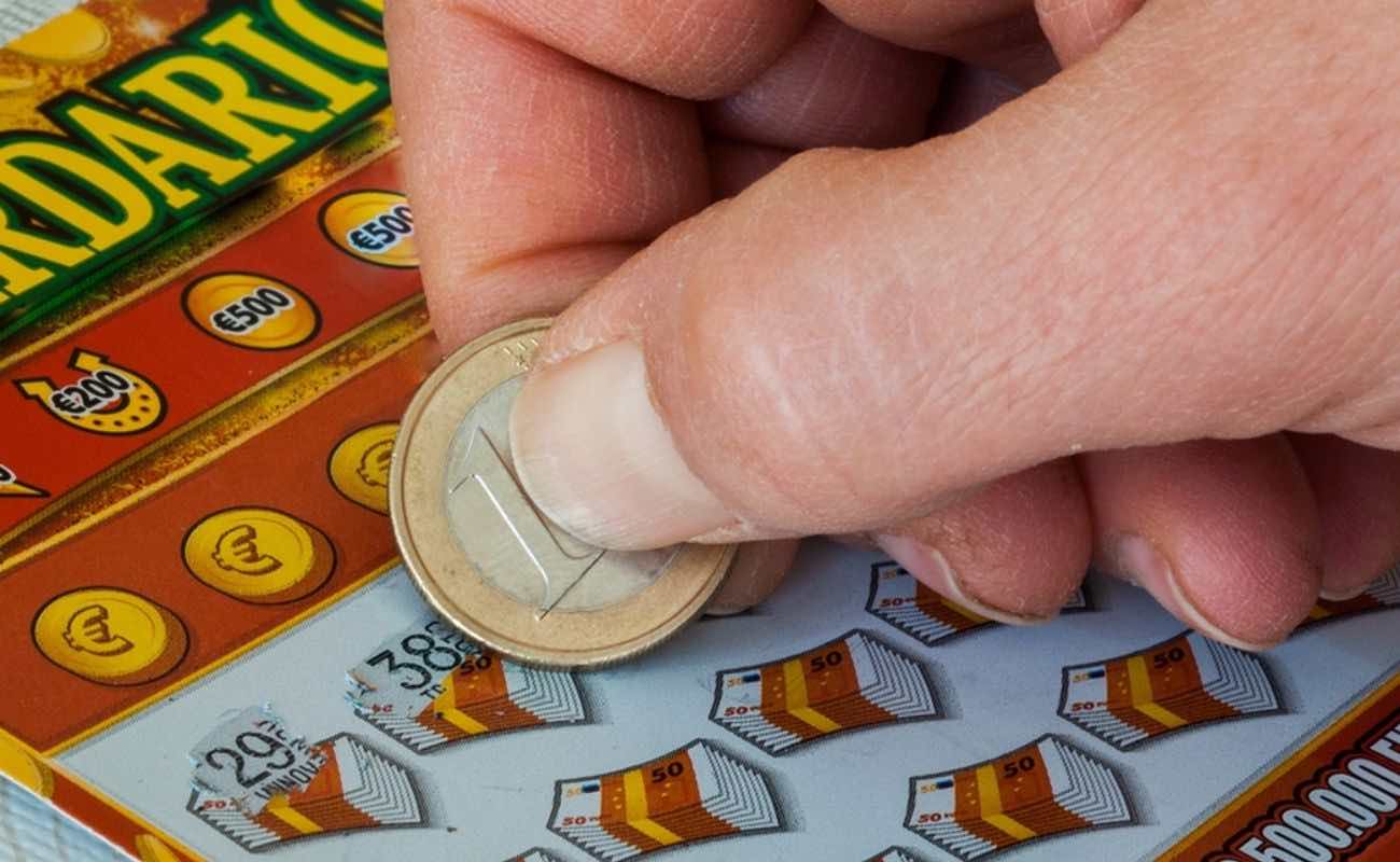 A hand uses a coin to reveal images on a European scratch card.